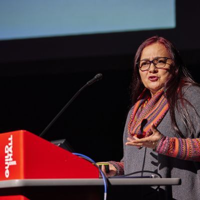 Colombian woman presenting in an animated style at a lectern with microphone